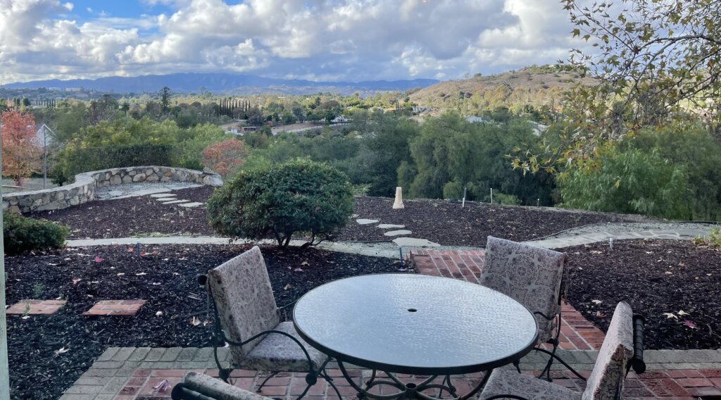Brick patio and mature trees with fall leaves at 145 Yucca Road in Fallbrook during a rainstorm.