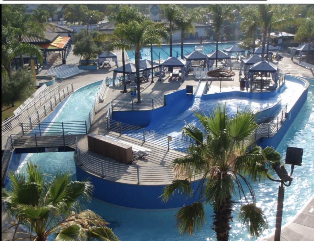 The Wave Waterpark in Vista, CA, showing the large, blue slide tower, flowing river, and pool area under a sunny sky. Highlights summer recreation and family fun in the city.